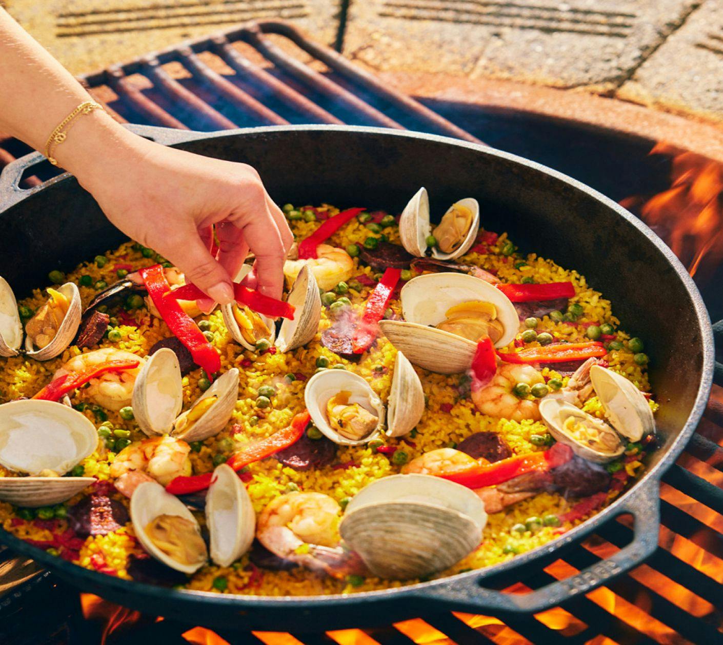 Paella pan on grill with peppers, clams, and saffron rice