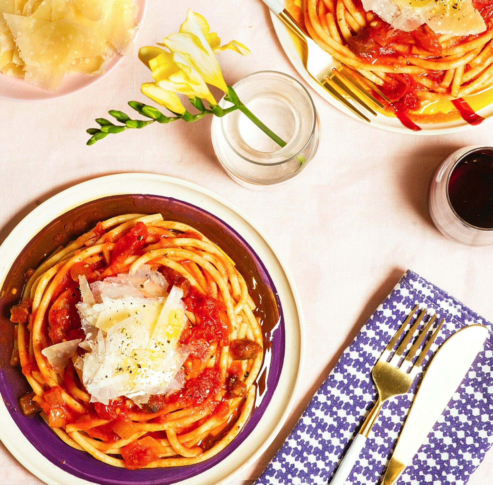 a table setting with 2 plates of spaghetti with red sauce and shaved cheese on top